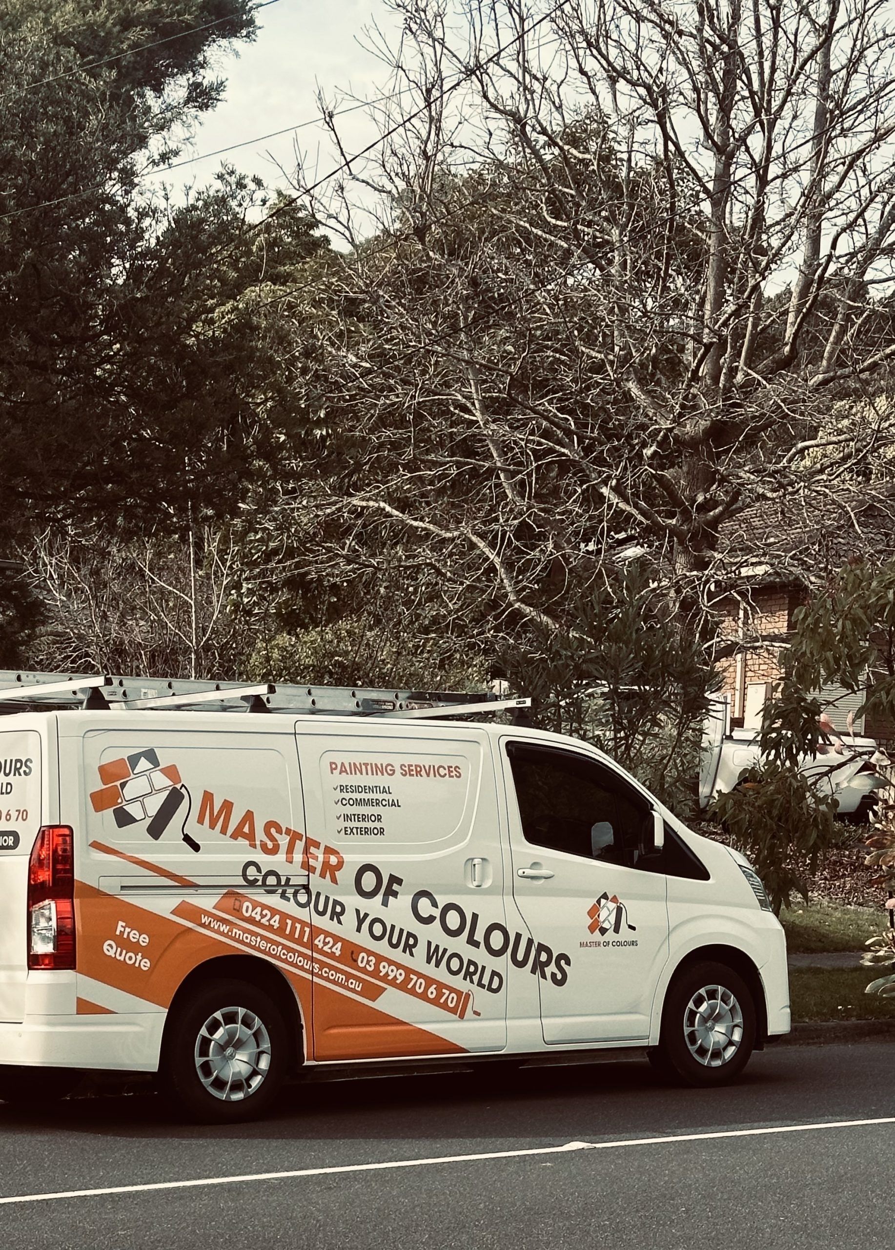 White painting service van with a roof ladder, parked on a street beside trees; branding reads Master of Colours with orange graphics.